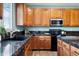 Close-up of a kitchen with wooden cabinets, black appliances, granite countertops, and a stainless steel sink at 9745 Hummingbird Pl, Littleton, CO 80125