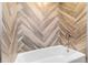 Modern bathroom featuring elegant herringbone-patterned tile, white bathtub, and stylish fixtures at 10380 W Warren Ave, Lakewood, CO 80227