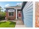 Inviting front entrance featuring a well-kept garden, brick accents, and a pop of color from the red door at 7061 Palisade Dr, Highlands Ranch, CO 80130