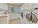 Bright laundry room with white cabinets, tile flooring, a utility sink, and modern appliances at 1127 Buttermilk Rd, Larkspur, CO 80118