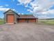 Large four-door garage with light green siding, rock accents, and gravel parking area at 1660 Prominence Cir, Elizabeth, CO 80107
