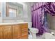 Modest bathroom featuring wood vanity, mirror, toilet, and shower with purple curtain at 9400 W Burgundy Ave, Littleton, CO 80123