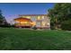 Expansive backyard at dusk with a large green lawn, a covered deck with lights on, mature trees, and a hot tub at 10085 Charissglen Ct, Highlands Ranch, CO 80126