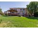 Expansive backyard with a large green lawn, a covered deck, mature trees, and a hot tub at 10085 Charissglen Ct, Highlands Ranch, CO 80126