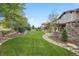 Well-manicured backyard featuring green grass, mature trees, and a stone outdoor kitchen at 10738 Braesheather Ct, Highlands Ranch, CO 80126