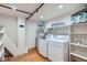 Functional laundry room equipped with modern washer, dryer, shelving, and exposed pipes at 2715 Blake St # 2, Denver, CO 80205