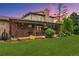 View of the covered patio, brick chimney, landscaped yard, complete with beautiful flowers and a lush lawn at 5954 W Leawood Dr, Littleton, CO 80123