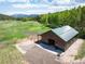 Aerial view of barn with an asphalt drive, metal roof, fencing, and pasture, surrounded by trees and mountains at 11652 Camp Eden Rd, Golden, CO 80403