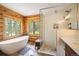 This primary bathroom features a soaking tub beneath a large window, a tiled shower with glass doors, and wood paneled walls at 11652 Camp Eden Rd, Golden, CO 80403