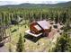 Aerial view of a wood-sided home with a deck, encircled by a lush green lawn and verdant forest at 11652 Camp Eden Rd, Golden, CO 80403