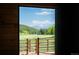 Scenic view from inside a barn featuring a meadow, green forest, and snow-capped mountains on a clear day at 11652 Camp Eden Rd, Golden, CO 80403