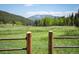 Open pasture view framed by split rail fence and lush forest with view of distant mountains at 11652 Camp Eden Rd, Golden, CO 80403