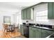 Well-lit kitchen with green cabinets, black countertops, and a view into a dining area at 6982 Estes Dr, Arvada, CO 80004