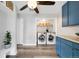 Bright laundry room with dual stainless steel washer and dryer, open shelving and blue cabinetry at 18143 E 104Th Way, Commerce City, CO 80022