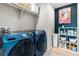 Laundry room with blue front-load washer and dryer, shelving, art, and tan tile flooring at 502 Green Mountain Dr, Erie, CO 80516