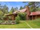 Picturesque cabin featuring a stone chimney, red roof, wooden beams, covered deck and green lawn at 245 N County Highway 67, Sedalia, CO 80135