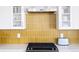 Focus on the kitchen backsplash, a unique golden color made of vertical tiles and white cabinetry at 2321 S Acoma St, Denver, CO 80223