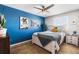 Bedroom featuring a striking blue accent wall, whitewashed wood bed frame, ceiling fan, and shuttered window at 14110 Pastel Ln, Parker, CO 80134