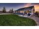 Exterior of home at dusk, featuring a large lawn, patio with seating, and fenced-in backyard at 11560 Kalispell St, Commerce City, CO 80022