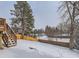 Snowy backyard with wooden deck and tall trees at 1218 Ascot Ave, Highlands Ranch, CO 80126