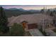 Beautiful exterior view of a stone home with a wooden garage door nestled amongst the mountains at dusk at 1015 Nob Hill Rd, Evergreen, CO 80439