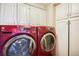 Well-lit laundry room featuring red front load washer and dryer units, and bright white cabinets for ample storage at 1900 E Girard Pl # 608, Englewood, CO 80113