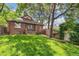 View of a brick home's backyard featuring mature trees, a manicured lawn, and a privacy fence at 3055 N Albion St, Denver, CO 80207