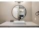 A bathroom vanity with a white countertop, white sink, black hardware, and round mirror at 16392 Spanish Peak Way, Broomfield, CO 80023