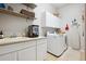 Bright laundry room with a sink, white cabinets, washer, dryer, and open shelving for storage at 1488 Baguette Dr, Castle Rock, CO 80108