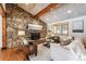 Cozy living room features a stone fireplace, wood floors, beams, and comfortable seating with natural light at 9019 Armadillo Trl, Evergreen, CO 80439