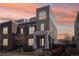 Modern two-story townhome featuring brick and stucco exterior, landscaping, and covered entry at sunset at 5438 Valentia St, Denver, CO 80238