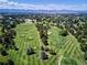 An aerial view of a pristine golf course showcasing lush green fairways, mature trees and mountain views at 5254 W Oberlin Dr, Denver, CO 80235