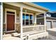 Charming front porch with brown door, large windows, stone accents, white pillars and porch swing at 56607 E 23Rd Ave, Strasburg, CO 80136