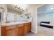 Bathroom with double sinks, wood cabinets, and tiled backsplash, with a peek into bedroom at 7734 Terry Ct, Arvada, CO 80007