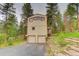 Exterior view of home's front, featuring 2-car garage, tall trees, and partial stone retaining wall at 9209 William Cody Dr, Evergreen, CO 80439