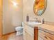 Well-lit bathroom featuring a wood cabinet, tan tile countertop, decorative oval mirror, and a toilet at 11766 Coal Creek Heights Dr, Golden, CO 80403