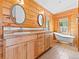 Bathroom featuring double sinks, wood paneling, and a clawfoot tub with a view of the trees outside at 11766 Coal Creek Heights Dr, Golden, CO 80403