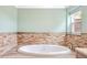 Relaxing soaking tub featuring tiled accent wall and window view, for a spa-like bathroom experience at 6891 W Eldorado Pl, Lakewood, CO 80227