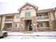 Exterior of the building with stone accents, multiple floors, and balconies covered in light snow at 10487 W Hampden Ave # 101, Lakewood, CO 80227