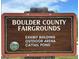Brown Boulder County Fairgrounds sign, listing the Exhibit Building, Outdoor Arena, and Cattail Pond at 301 Widgeon Ln, Longmont, CO 80503