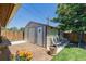 Exterior view of storage shed with double doors, patio, and chairs, surrounded by landscaping at 9170 Aspen Dr, Thornton, CO 80229