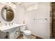 Well-lit bathroom featuring a pedestal sink, round mirror, and toilet in a neutral color palette at 1795 N Monaco St Pkwy, Denver, CO 80224
