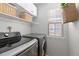 A modern laundry room featuring a gray washer and dryer, white cabinets, woven baskets, and a window for natural light at 9810 Mulberry Way, Highlands Ranch, CO 80129