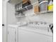 Functional laundry room with white appliances and overhead shelving for storage and organization at 12606 Fairfax St, Thornton, CO 80241