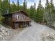 Exterior view of a two-story cabin in a forest with a large deck and gravel driveway at 159 Lake Rd, Idaho Springs, CO 80452
