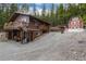 Cozy two-story cabin with a deck and red barn surrounded by a lush forest and a gravel driveway at 159 Lake Rd, Idaho Springs, CO 80452