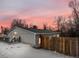 This home features gray siding, wood fence, and snow covered yard at dusk at 3398 Wadsworth Blvd, Wheat Ridge, CO 80033