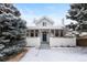 Charming bungalow featuring a blue front door, white brick facade and snow-covered landscaping at 3438 N York St, Denver, CO 80205