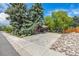 Spacious driveway with a two-car garage and a landscaped area featuring rocks and mature trees at 5365 W Princeton Dr, Denver, CO 80235