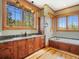 Bathroom features dual sink vanity, soaking tub, wood trim, and large windows with a scenic view at 3395 Timbergate Trl, Evergreen, CO 80439